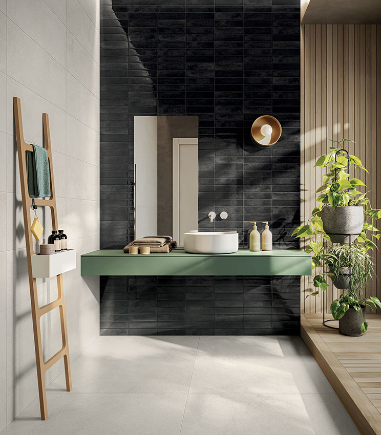 Contemporary bathroom featuring surfaces from the La Matière Talc and Workshop Core collections, with a glossy dark wall, light-toned surfaces, a floating green vanity, wooden details and several plants lit by natural light.