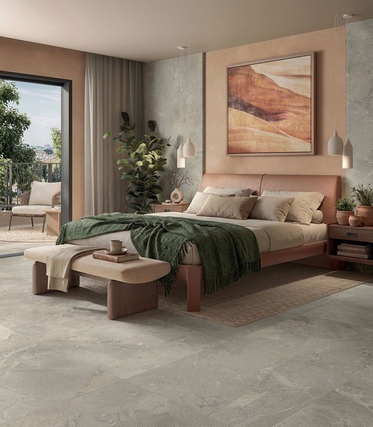 Contemporary bedroom featuring surfaces from the Revel Ground collection, with stone-effect flooring and wall coverings, an upholstered bed in dusty pink tones, neutral and dark green textiles, wooden bedside tables and a wide opening onto a bright terrace.