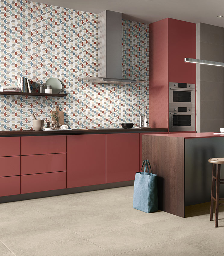 Contemporary kitchen featuring surfaces from the Even Dove, Optical Terzofuoco and Context Square collections, with a multicoloured geometric wall covering, terracotta cabinetry, dark worktop, central island and light flooring.