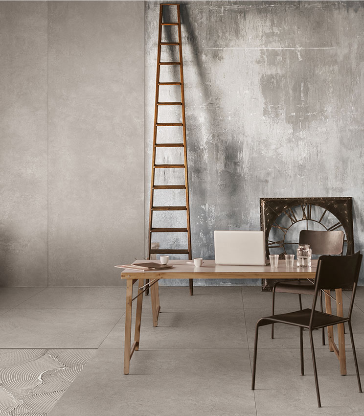 Industrial-style office space with concrete-effect flooring, textured walls, wooden staircase, and minimalist furnishings in wood and metal.