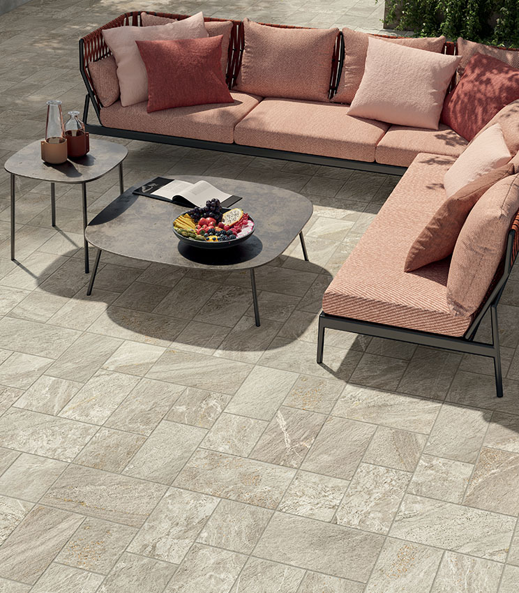 Top view of an outdoor lounge area with pink fabric seating and metal coffee tables. Stone-effect porcelain stoneware flooring laid in a multi-format pattern.