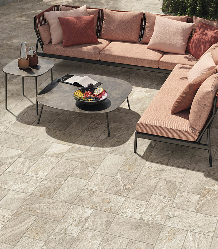 Vista dall'alto di un salotto outdoor in tessuto di colore rosa con tavolini in metallo. Pavimento in gres porcellanato effetto pietra posato con modulo multiformato