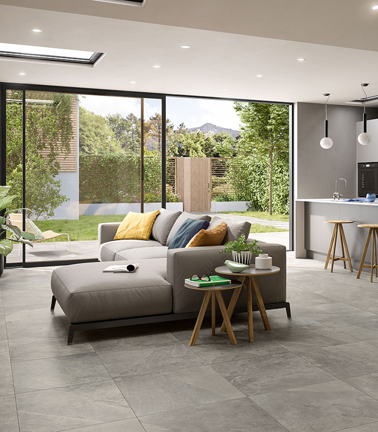 View of open-plan living room and kitchen with large glass door overlooking a small private garden. Grey stone-effect porcelain stoneware flooring.