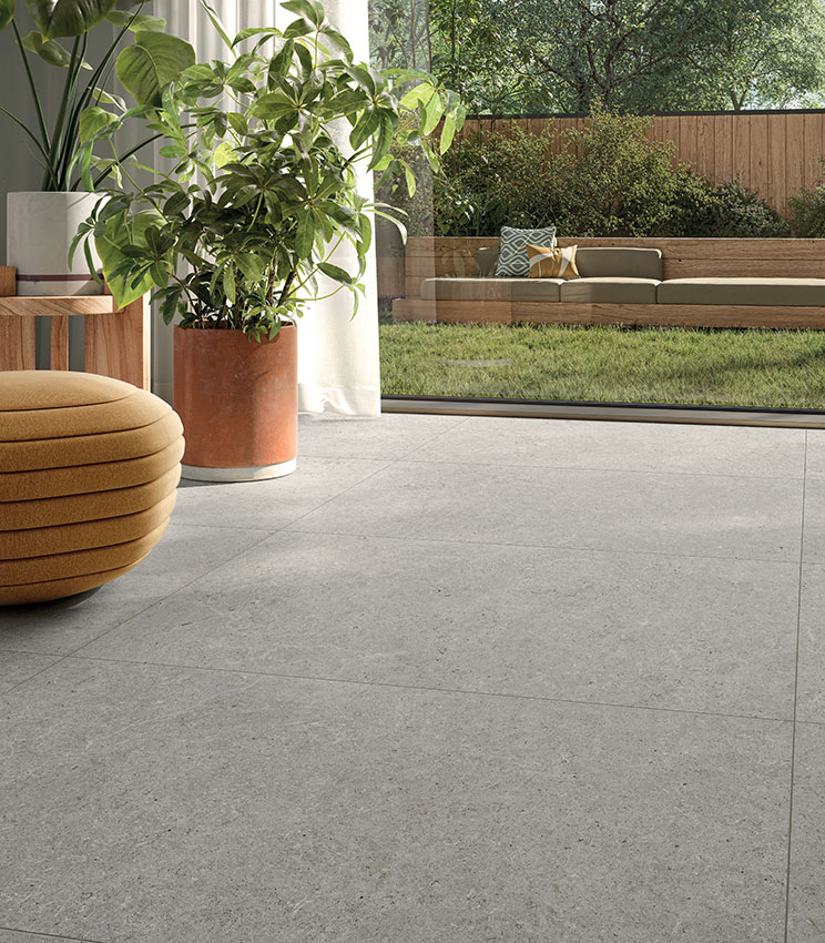 Zona living con vista sul giardino e pavimento in gres chiaro Surround di Panaria Ceramica, per una continuità tra interno ed esterno.