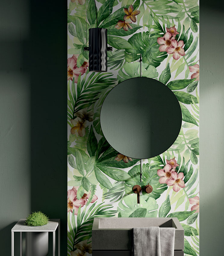 Contemporary bathroom featuring decorative wall covering from the Glam Rainforest collection, with a tropical pattern of large green leaves and pink flowers. The space includes dark green walls, a geometric washbasin, round mirror, wall-mounted tapware and a black pendant light.