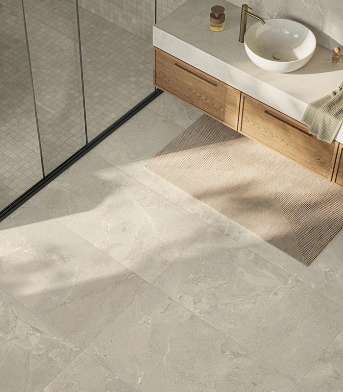 Top view of a light-coloured stone-effect porcelain stoneware floor, featuring a matching small-format mosaic shower tray and a glimpse of a wall-mounted wooden washbasin unit.