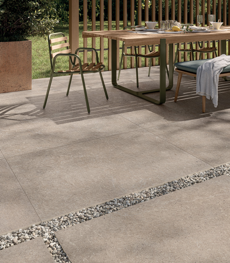 View of a breakfast patio laid with 20 mm outdoor stone-effect porcelain stoneware in a sand colour, partly adhesive-laid and partly dry-laid on gravel | Surround collection by Panaria Ceramica