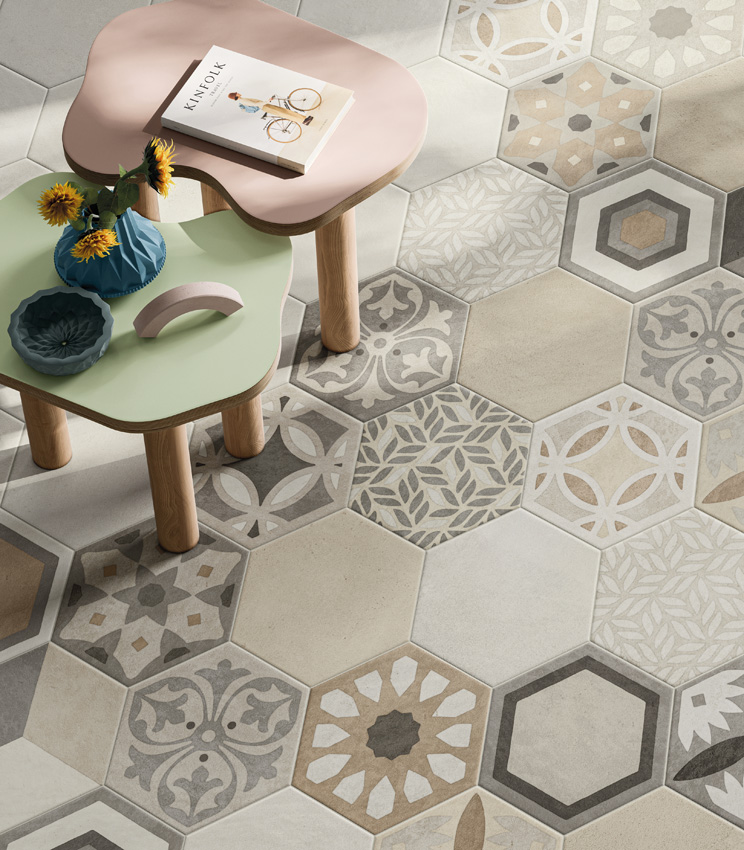 Overhead view of a light concrete-effect hexagonal porcelain stoneware floor with two low coloured coffee tables and a large section of decorative geometric and foliage motifs typical of artisanal hexagonal tiles.