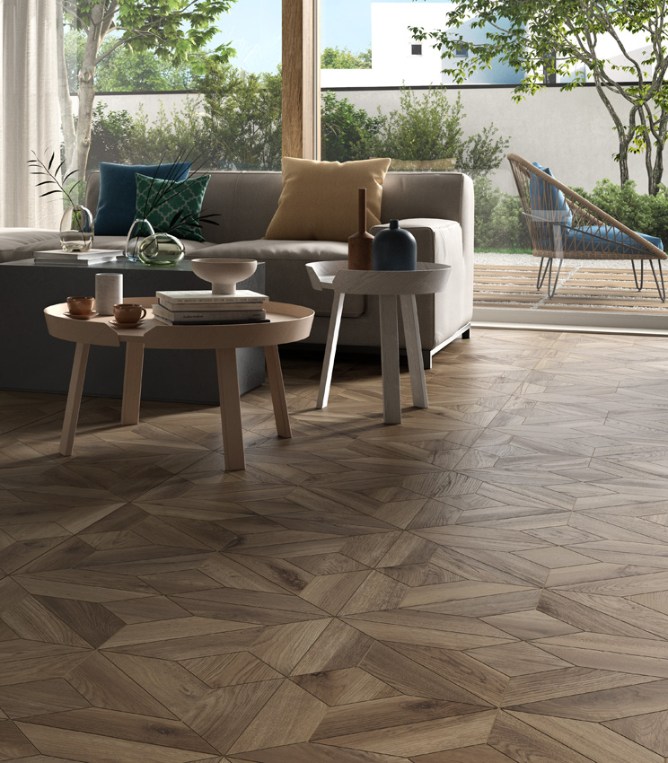 View of a living area with large glazed windows and two oversized sofas, featuring a dark wood-effect porcelain stoneware floor laid in a coffered pattern.