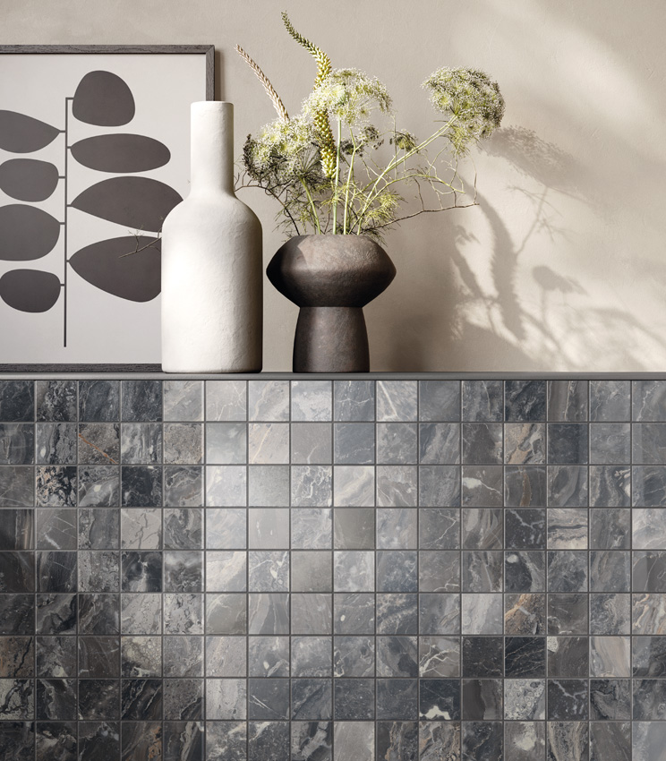 Close-up front view of a low wall with a shelf holding two vases and an abstract painting. The low wall is clad in dark marble-effect ceramic mosaic while the rest of the wall is painted ivory.