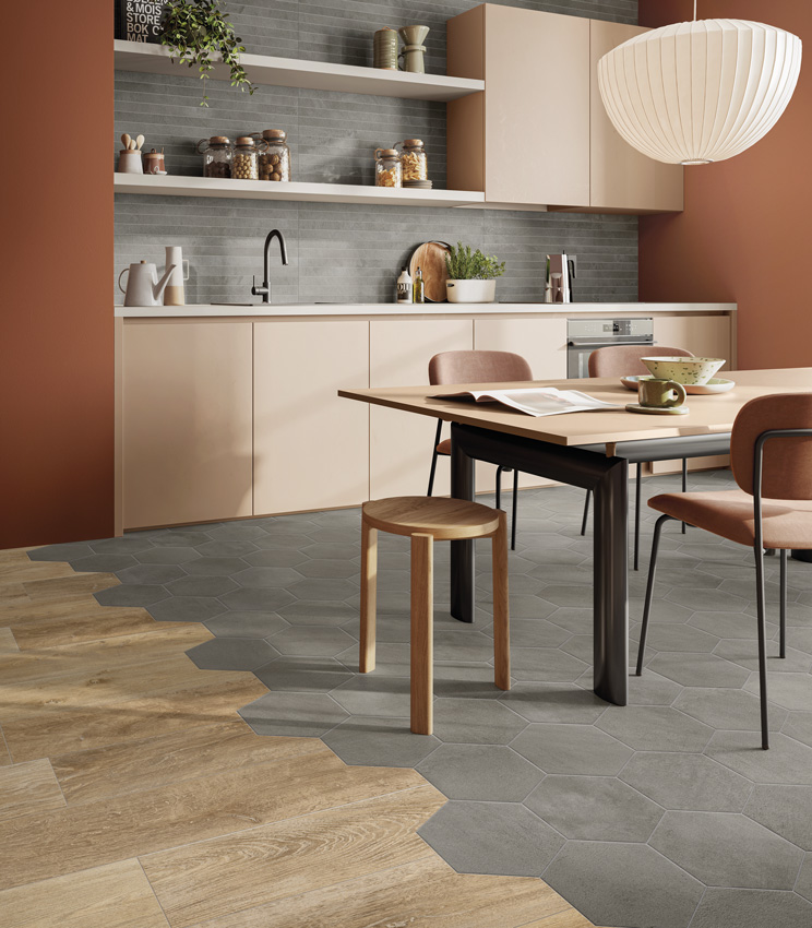 View of a modern kitchen with brick-red painted walls and powder-pink cabinetry, a backsplash in grey concrete-effect porcelain stoneware strips and a multi-effect floor combining ceramic concrete hexagonal tiles and wood-effect porcelain stoneware planks.