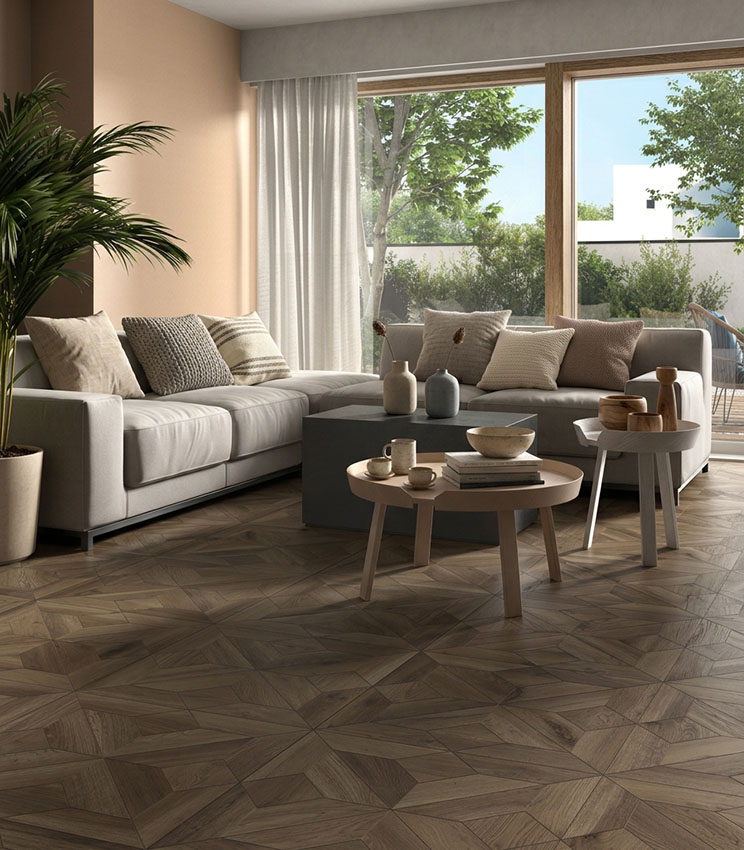 Contemporary living room featuring flooring from the Borealis Donegal Baroque collection, with a geometric wood-effect pattern, a large light-coloured sofa, low coffee tables, neutral tones and floor-to-ceiling windows overlooking greenery.